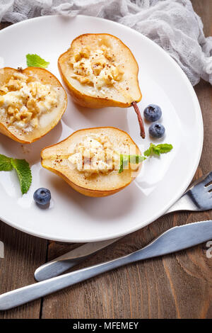 Pears baked with Ricotta cheese, nuts, honey and cinnamon on rustic wooden background Stock Photo