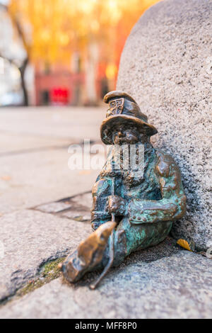 Small copper statue of a dwarf, sitting on the floor of a street in Wroclaw, Poland. Wrocław’s dwarfs are famous tourist attraction in the city. Stock Photo