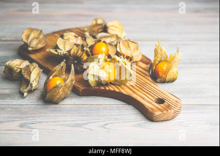 Physalis on a cutting board on a wooden background. Light toning Stock Photo