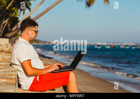 Man working with a laptop, on a hammock in the beach. Concept of digital nomad, remote worker, independent location entrepreneur. Stock Photo