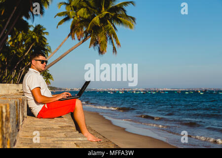 Man working with a laptop, on a hammock in the beach. Concept of digital nomad, remote worker, independent location entrepreneur. Stock Photo