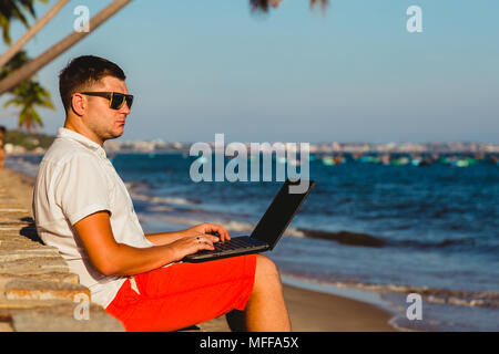 Man working with a laptop, on a hammock in the beach. Concept of digital nomad, remote worker, independent location entrepreneur. Stock Photo