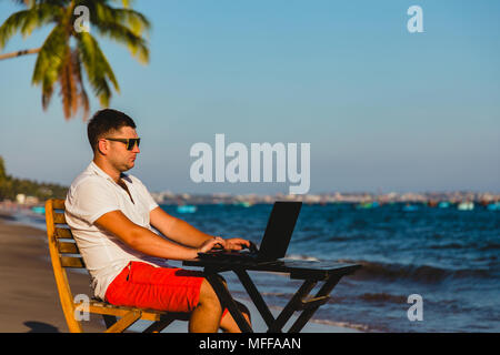 Man working with a laptop, on a hammock in the beach. Concept of digital nomad, remote worker, independent location entrepreneur. Stock Photo