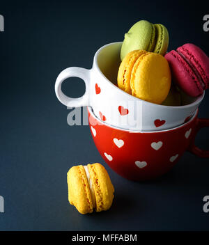 multicolored baked cakes of almond flour macarons in a white ceramic cup on a black background Stock Photo