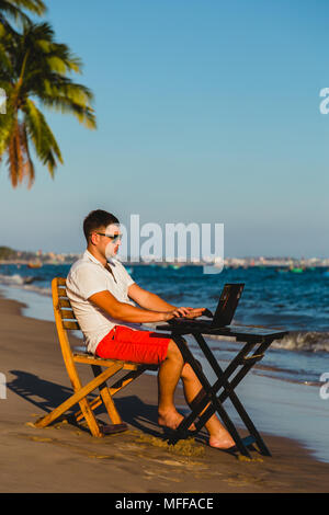 Man working with a laptop, on a hammock in the beach. Concept of digital nomad, remote worker, independent location entrepreneur. Stock Photo