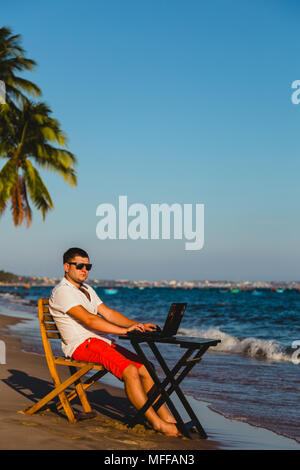 Man working with a laptop, on a hammock in the beach. Concept of digital nomad, remote worker, independent location entrepreneur. Stock Photo
