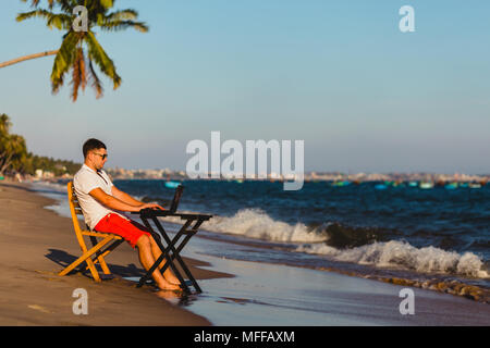 Man working with a laptop, on a hammock in the beach. Concept of digital nomad, remote worker, independent location entrepreneur. Stock Photo