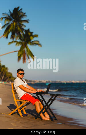 Man working with a laptop, on a hammock in the beach. Concept of digital nomad, remote worker, independent location entrepreneur. Stock Photo