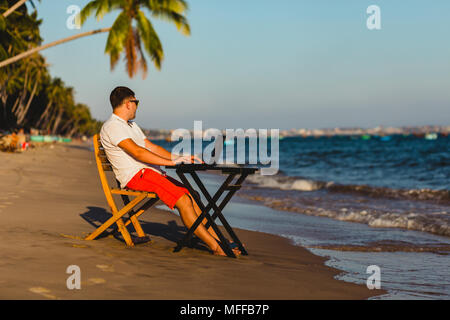 Man working with a laptop, on a hammock in the beach. Concept of digital nomad, remote worker, independent location entrepreneur. Stock Photo