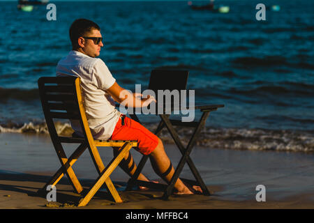 Man working with a laptop, on a hammock in the beach. Concept of digital nomad, remote worker, independent location entrepreneur. Stock Photo