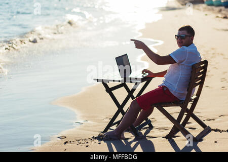 Man working with a laptop, on a hammock in the beach. Concept of digital nomad, remote worker, independent location entrepreneur. Stock Photo
