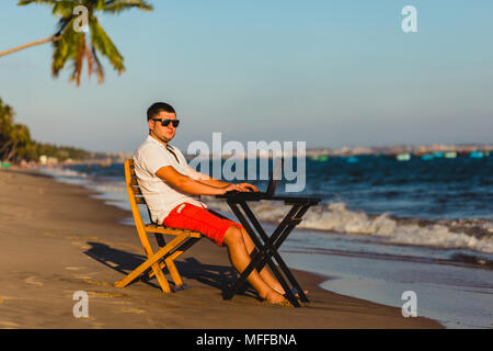Man working with a laptop, on a hammock in the beach. Concept of digital nomad, remote worker, independent location entrepreneur. Stock Photo
