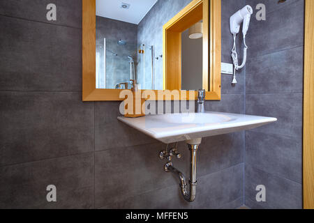White shiny sink with mirror in bathroom with gray tile on walls. Interior of modern bath.