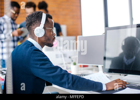 side view close up portrait of serious Afro student with headphones preparing for seminar in the university. write a graduation paper, course work Stock Photo