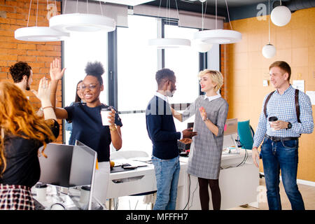 two diverse women are making high five, Caucasian man is looking at talking woman with fair hair with African man in break time Stock Photo