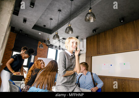 stylish blond secretary is laughing and talking with her boyfriend on mobile phone with co-workers on the background of the photo Stock Photo