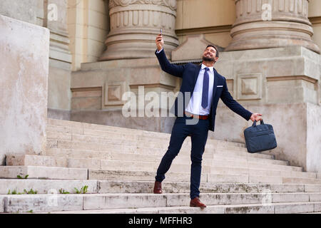 A handsome young businessman walking down on the stairs and celebrating Stock Photo