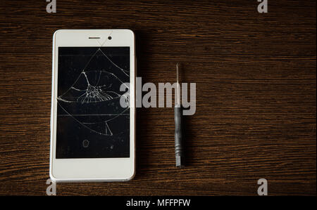 smart phone with broken screen on wooden background with small screwdriver for repair Stock Photo