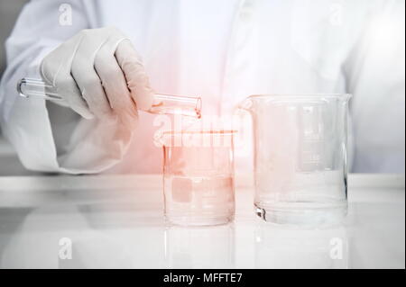 researcher in white lab coat holding cylinder and poring water into beaker in science laboratory experiment background Stock Photo