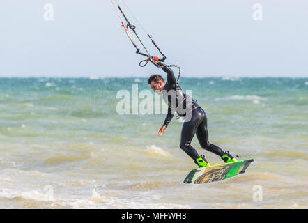 Man kitesurfing at sea and taking off while holding on with one hand. Kitesurfer on the ocean. Watersports. Stock Photo