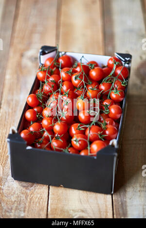Ripe Cherry tomatoes branches in a market cardboard box over a rustic wooden table. Stock Photo