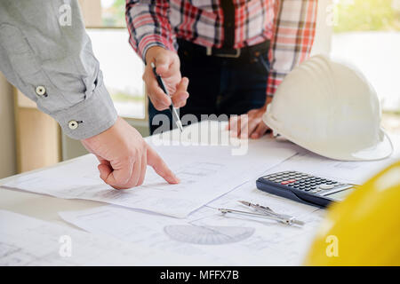 Engineers discuss a blueprint while checking information on a tablet computer in a office. Stock Photo