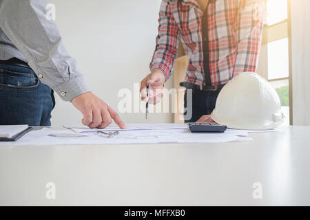 Engineers discuss a blueprint while checking information on a tablet computer in a office. Stock Photo