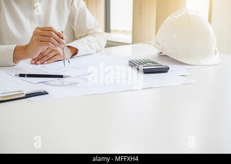 Engineers discuss a blueprint while checking information on a tablet computer in a office. Stock Photo