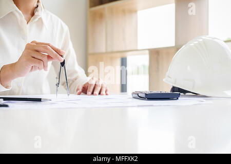 Engineers discuss a blueprint while checking information on a tablet computer in a office. Stock Photo