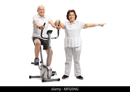 Mature man riding a stationary bike with a mature woman pointing isolated on white background Stock Photo