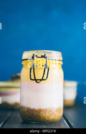 Ombre cheesecake on a jar glass made with three different layer of cheese, acai cream cheese , blueberry and mango pulp, top view on a gray table agai Stock Photo