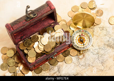 Open treasure chest filled with gold colored coins and compass over medieval world map Stock Photo