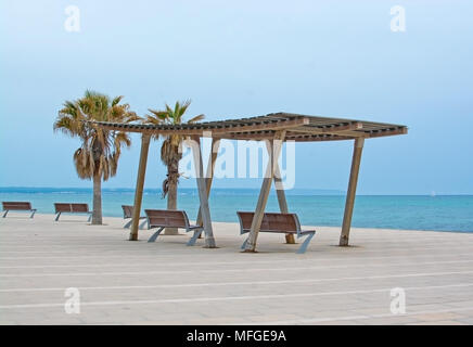 Wooden shade structure with seats, blue Mediterranean sea on an overcast day and horizon in Molinar, Mallorca, Spain. Stock Photo