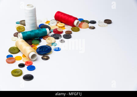 multi-colored buttons and coils with threads lie on a white surface Stock Photo