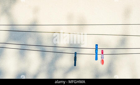Clothing pins hanging on washing lines with a clear wall as background, with copy space. Stock Photo