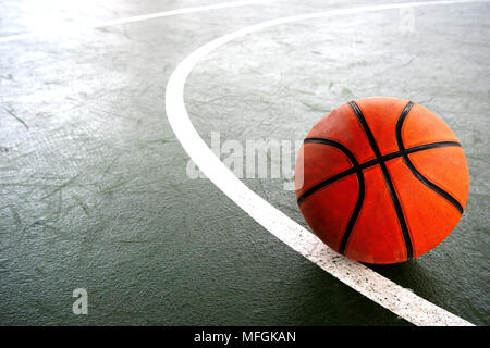single orange old basketball on dark green sport gymnasium with part of white circle line background Stock Photo