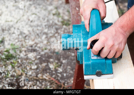 Close up hands of carpenter working with electric planer on wooden plank in carpentry workshop Stock Photo