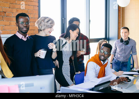 young African comercial laborer in glasses looking away next to his happy co-workers Stock Photo