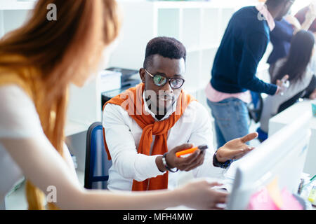 closeup portrait of puzzled black man in glasses sitting at workplace in front of computer in the modern office Stock Photo