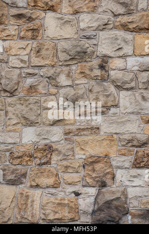 Building wall unevenly composed of earth-toned medium-size non-uniform rough-hewn stones of different shapes and sizes Stock Photo