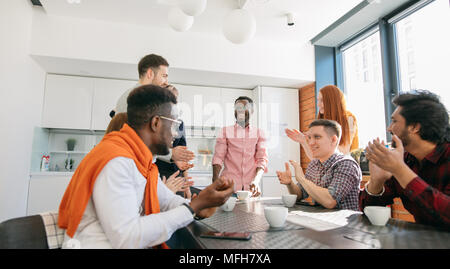old multiracial friends clapping hands and enjoying a chart over coffee in the loft kitchen Stock Photo