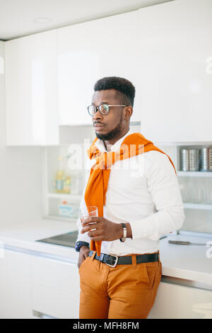 close-up side view portrait of handsome African man in glasses standing with glass of waterin the kitchen at home Stock Photo