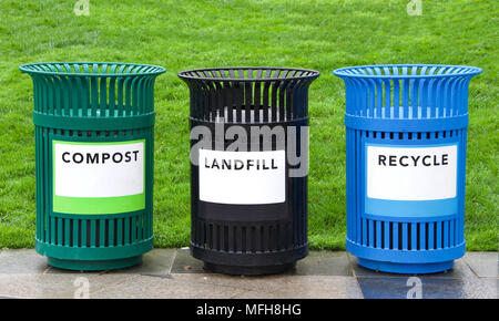 Variety of bright colorful trash cans in a park with grass in background. Green for Compost, black for landfill and blue recycling. copy space on labe Stock Photo