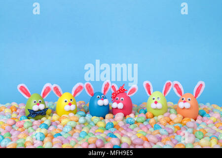 Craft Easter Bunnies made from plastic eggs standing in pastel jelly beans with a light blue background. Fun Easter line up with copy space Stock Photo