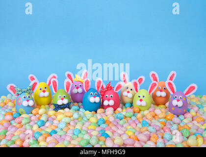 Craft Easter Bunnies made from plastic eggs standing in pastel jelly beans with a light blue background. Fun Easter line up with copy space Stock Photo