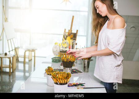 A young woman painter gently touching paintsbrushes on table missing after a long break in activity she likes Stock Photo