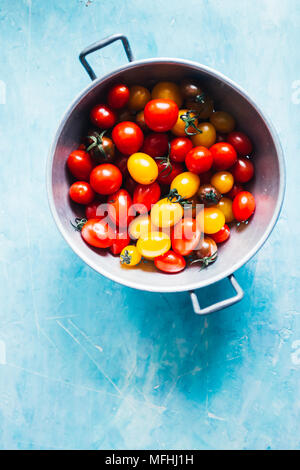 Freshly washed mixed cherry tomatoes inside a colander over a rusty granite blue background Stock Photo
