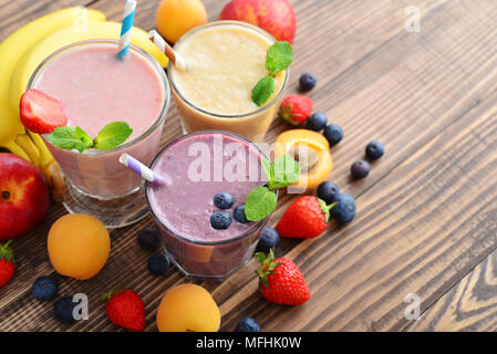 Three glass of fruit milkshakes or smoothies with drinking straws and fresh fruits and berries  on wooden background Stock Photo