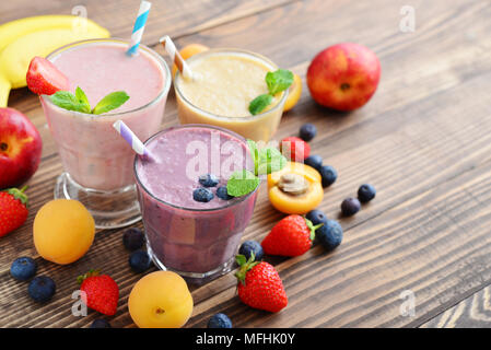 Three glass of fruit milkshakes or smoothies with drinking straws and fresh fruits and berries  on wooden background Stock Photo