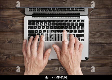 Working on laptop. Top view of man working on laptop laying on the wooden background. Stock Photo